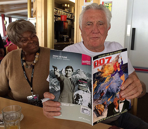 George Lazenby poses with a copy of 007 MAGAZINE while Sylvana Henriques looks on.