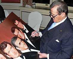 Sir Roger Moore signs a painting by Jeffrey Stamp